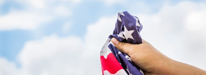 american-flag-held-by-hand-with-clouds-background